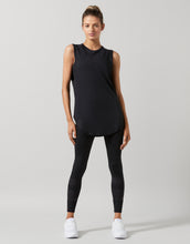 Woman wearing a black sleeveless top and leggings on a gray background