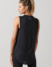 Woman wearing a black sleeveless top with a brand logo on a gray background
