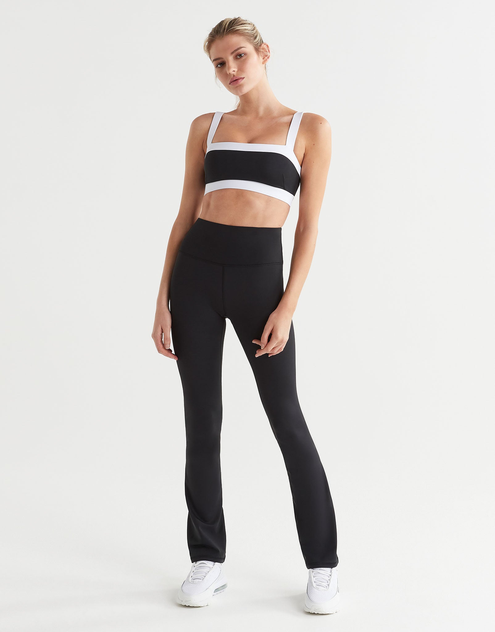 A model in a pair of high-waisted black bootcut leggings and a sports bra.