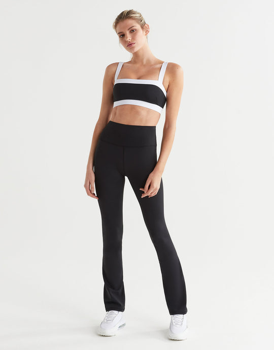 A model in a pair of high-waisted black bootcut leggings and a sports bra.