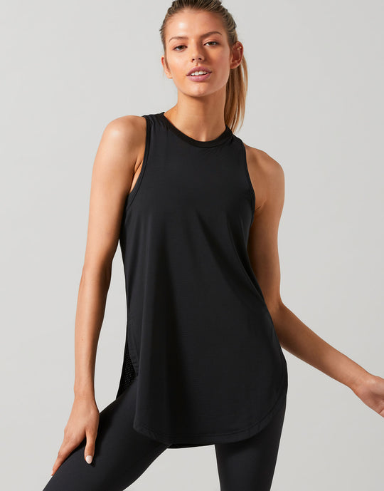 A woman wearing a black Lilybod Zela Mesh Tank Top with a wide scoop neck and dropped armholes, paired with black leggings.