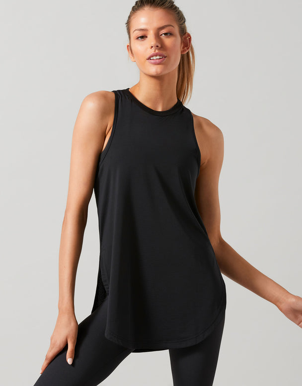 A woman wearing a black Lilybod Zela Mesh Tank Top with a wide scoop neck and dropped armholes, paired with black leggings.