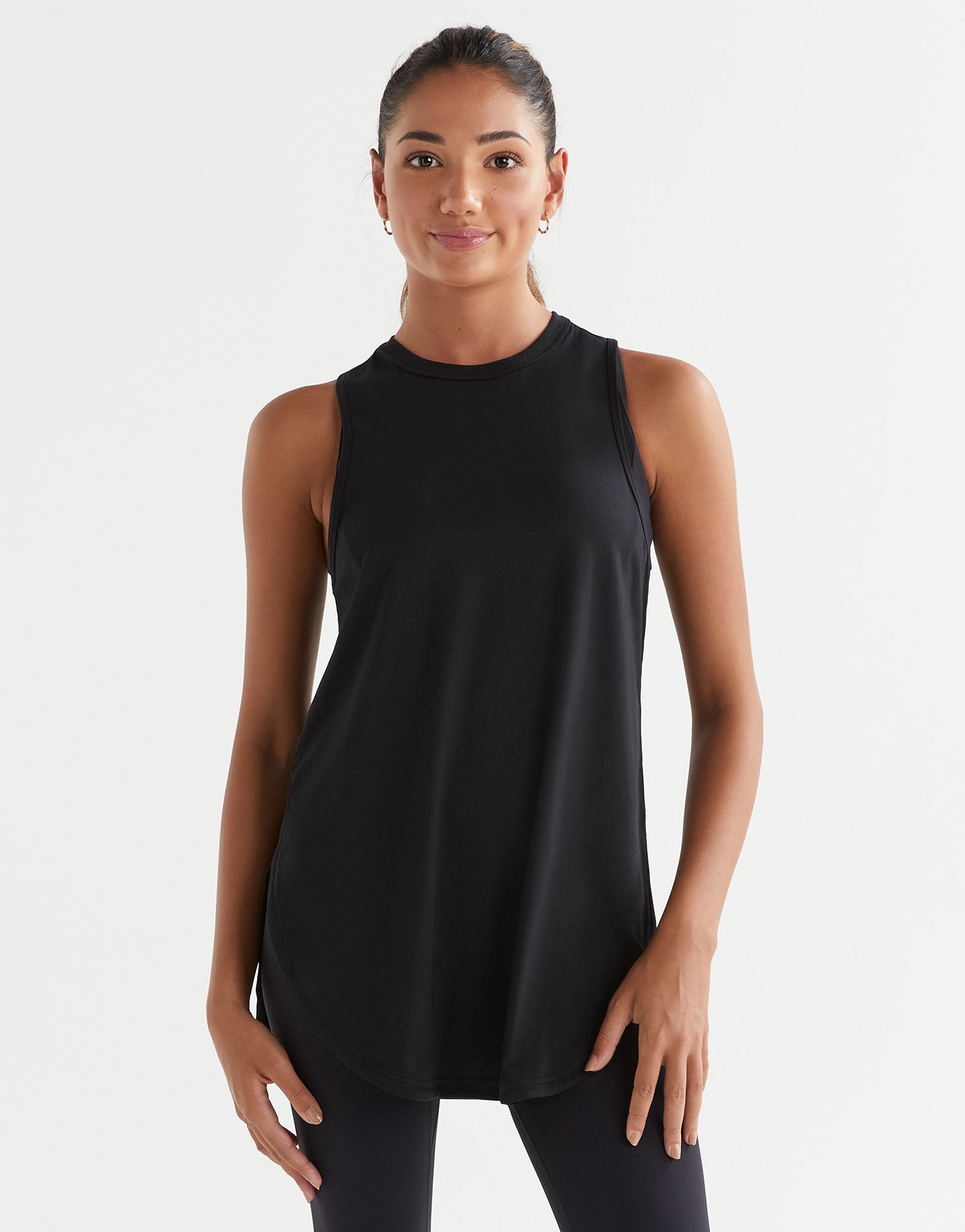 A woman standing, wearing a black sleeveless tank top with a wide scoop neckline and dropped armholes.