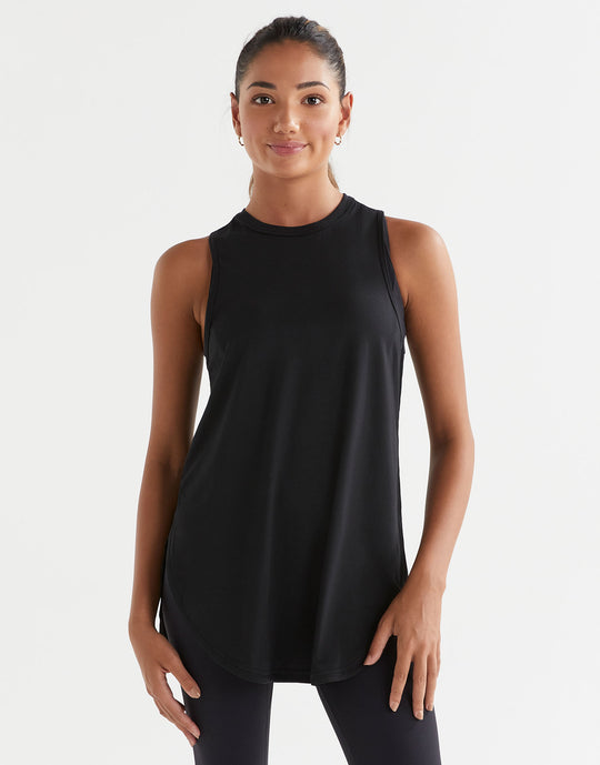 A woman standing, wearing a black sleeveless tank top with a wide scoop neckline and dropped armholes.