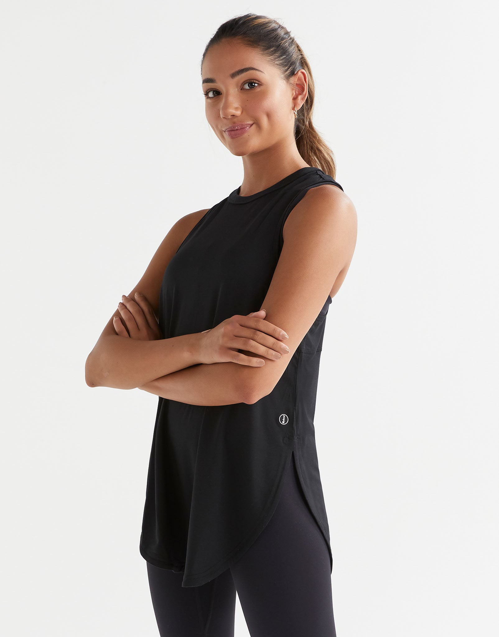 xA woman standing, wearing a black sleeveless tank top with a wide scoop neckline and dropped armholes and leggings.