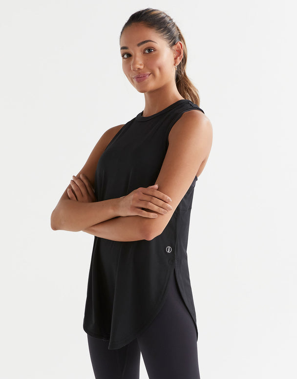 xA woman standing, wearing a black sleeveless tank top with a wide scoop neckline and dropped armholes and leggings.