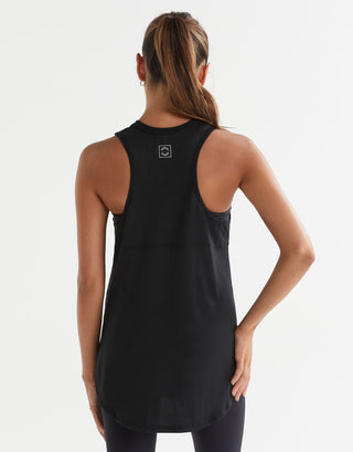 A model standing, wearing a black sleeveless tank top with a wide scoop neckline and dropped armholes.