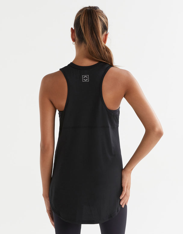 A model standing, wearing a black sleeveless tank top with a wide scoop neckline and dropped armholes.