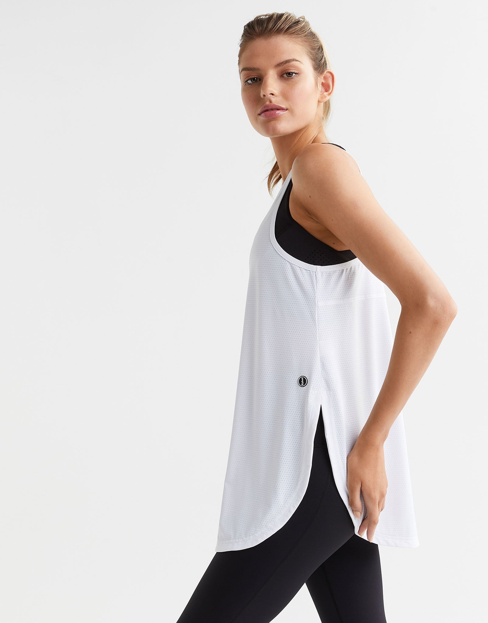Woman wearing a white sleeveless top and black leggings on a light gray background