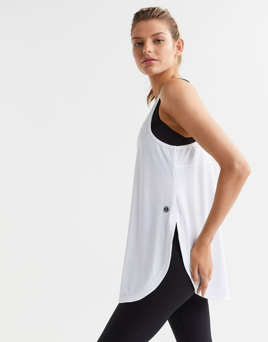 Woman wearing a white sleeveless top and black leggings on a light gray background