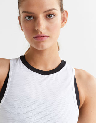 Woman wearing a white tank top with black trim on a plain background