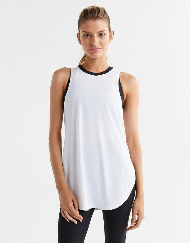 A woman wearing a white soft tank top and black leggings.