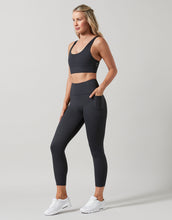 Woman wearing a black sports bra and leggings on a light gray background