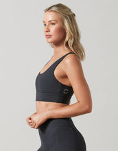 Woman wearing a black sports bra with a logo on a gray background