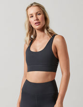 Woman wearing a black sports bra and leggings on a light gray background