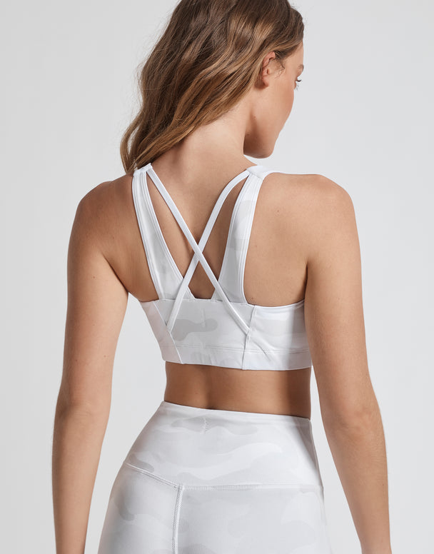 Woman wearing a white sports bra and leggings on a plain background