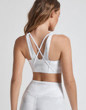 Woman wearing a white sports bra and leggings on a plain background