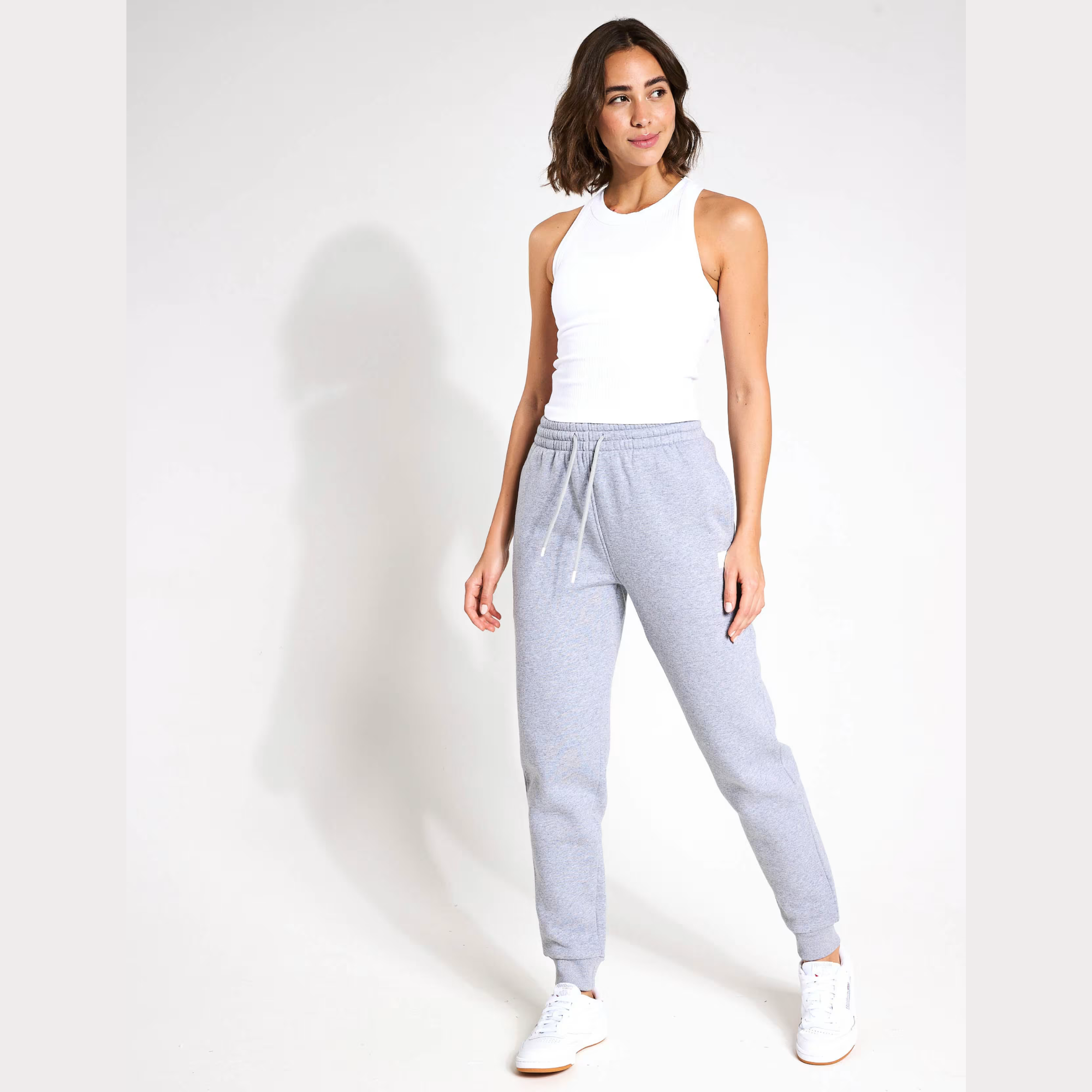 Woman wearing light grey sweatpants and a white sleeveless top on a white background