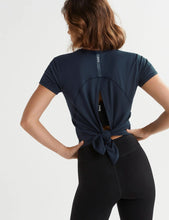 Person wearing a navy blue athletic top with a knot detail on the back, on a light gray background.