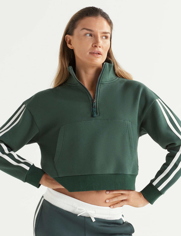 Woman wearing a green cropped hoodie with white stripes on the sleeves against a white background