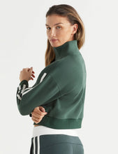 Woman wearing a green tracksuit with white accents on a light gray background